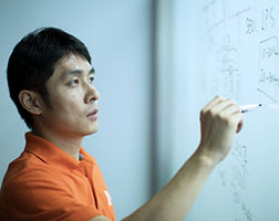 Image of a person in an office meeting environment, writing on a dry erase board.