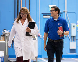 Image of two people walking down a laboratory hallway holding clipboards.