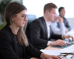 Image of multiple people in a boardroom environment working on their laptops.