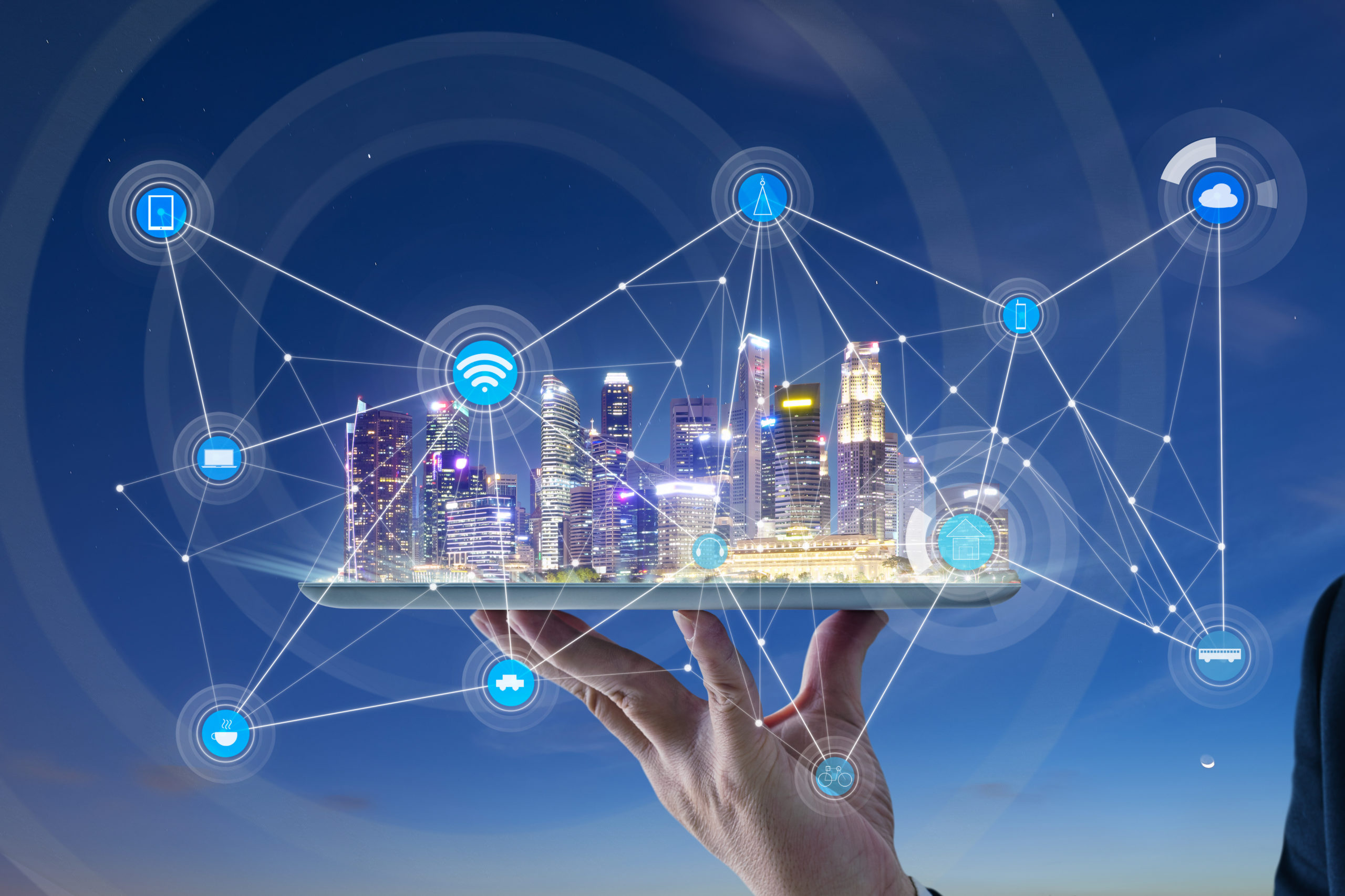 Featured Image. Hand holding a digital tablet with a city with smart services and icons, internet of things, and networks appearing from the tablet