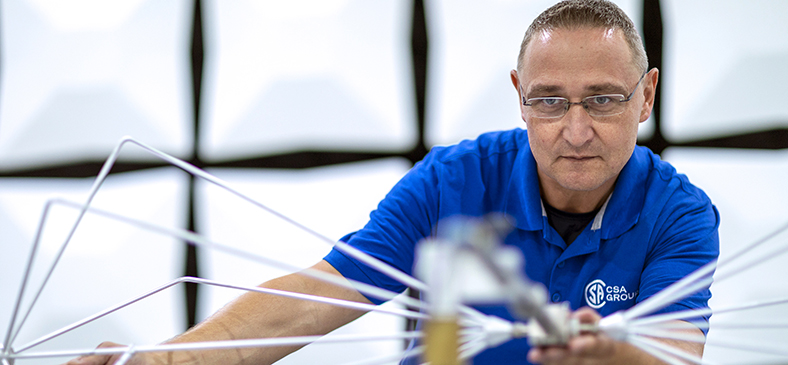 Featured Image. Technician wearing a blue shirt with the white CSA logo on it, setting up an antenna for EMC testing.
