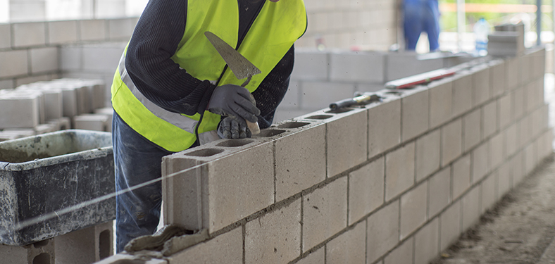 Featured Image. A construction worker layering concrete blocks on top of each other.