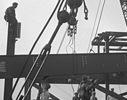 Image en noir et blanc de travailleurs sur un pont ferroviaire en acier.