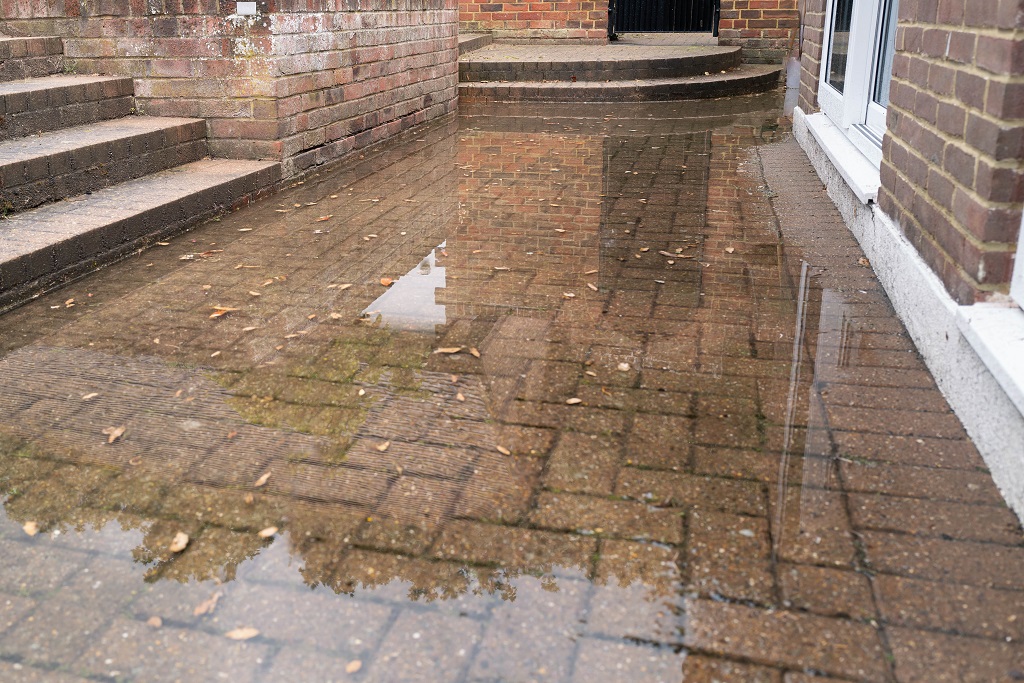 Featured Image. Brick patio area flooded after heavy rain due to a blocked soakaway