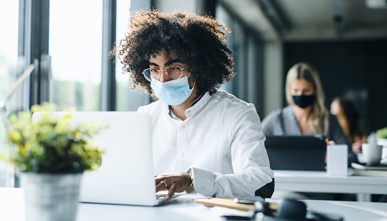 Featured Image. Employee wearing a face mask while working socially distanced in the office